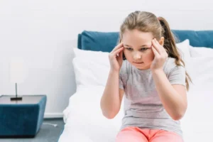 Cognitive stimulation in children with hydrocephalus. Girl touching her head with both hands.