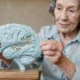 Older woman holding a brain-shaped puzzle and trying to fit a piece, highlighting brain connectivity.