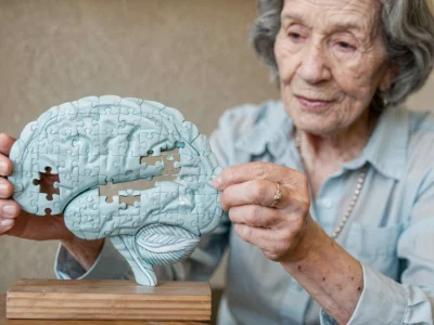 Older woman holding a brain-shaped puzzle and trying to fit a piece, highlighting brain connectivity.